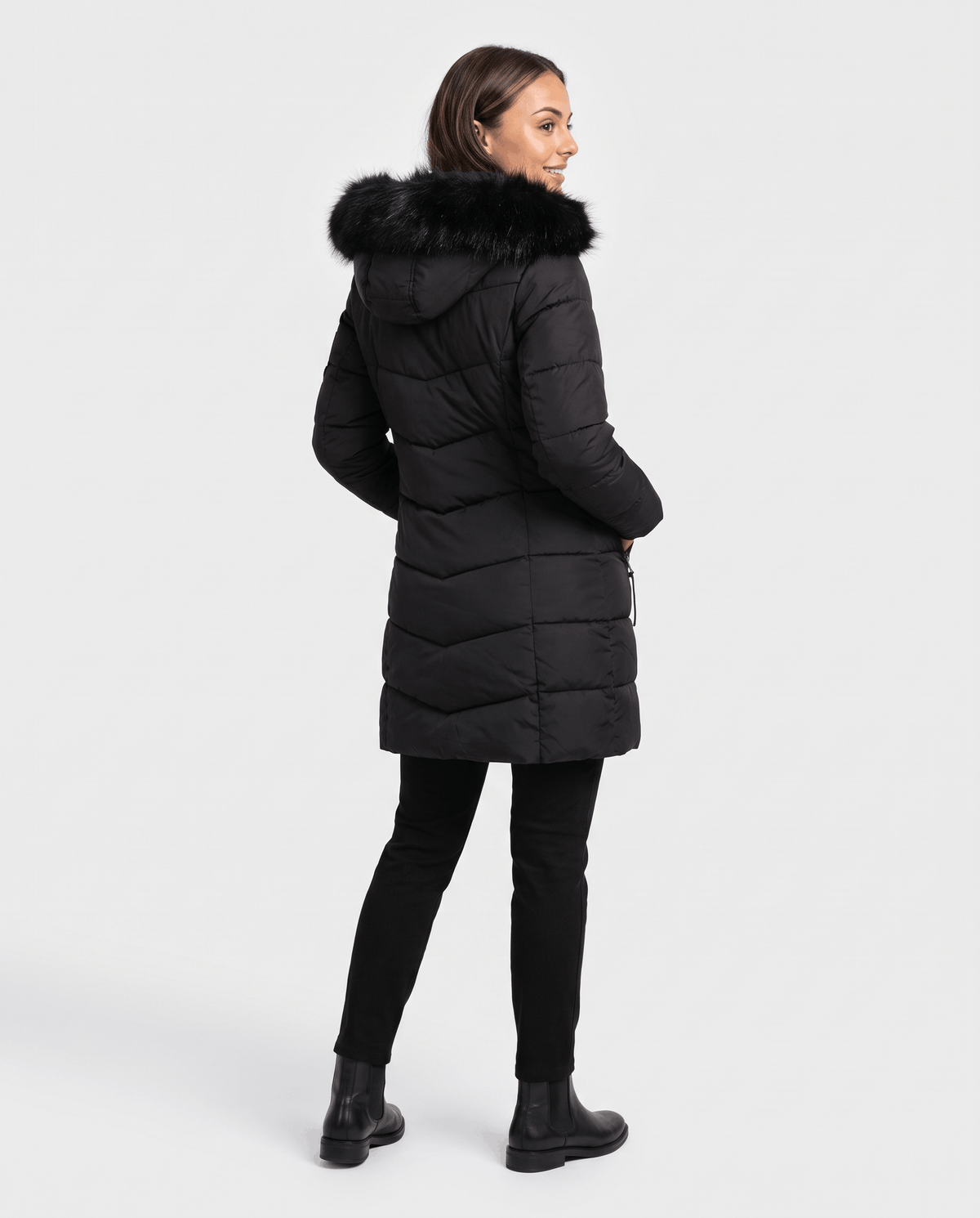 A woman wearing a black long insulated parka jacket with a hood and full-zip front, shown from the back
