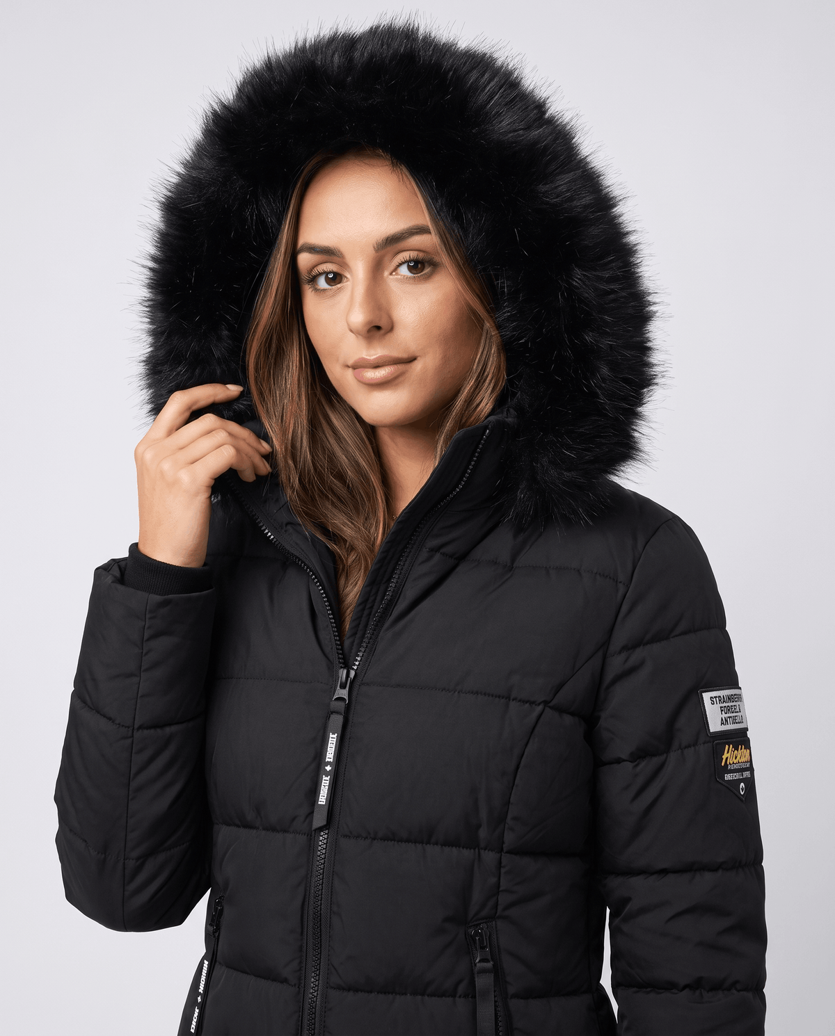 Close-up of a woman wearing a black long insulated parka jacket, showing the fur-trimmed hood and quilted design