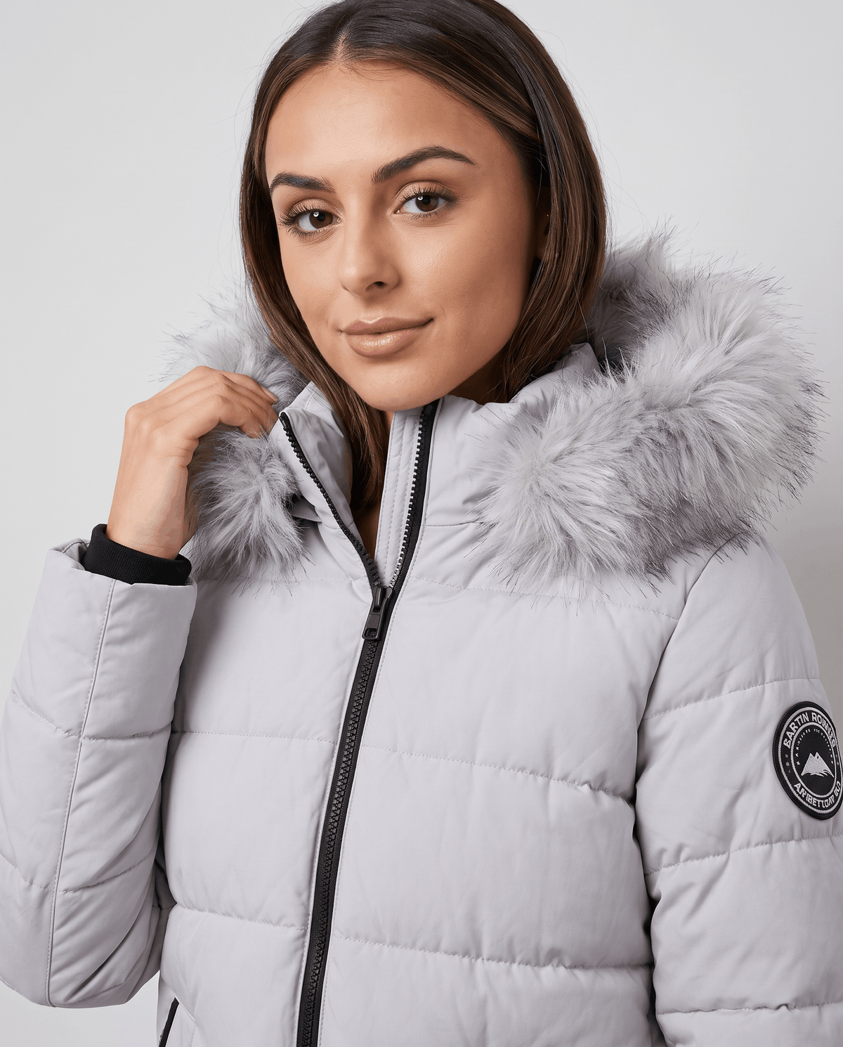 A woman wearing a light gray long insulated parka jacket with a hood and full-zip front