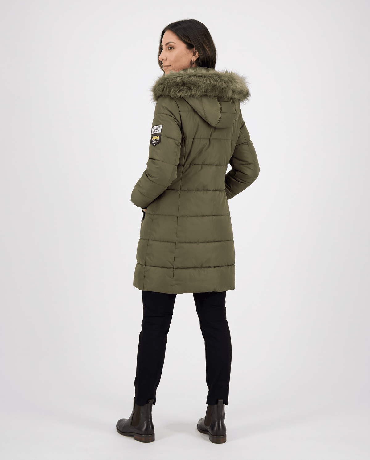 A woman wearing a long olive green parka jacket with an insulated hood and full-zip front, shown from the back
