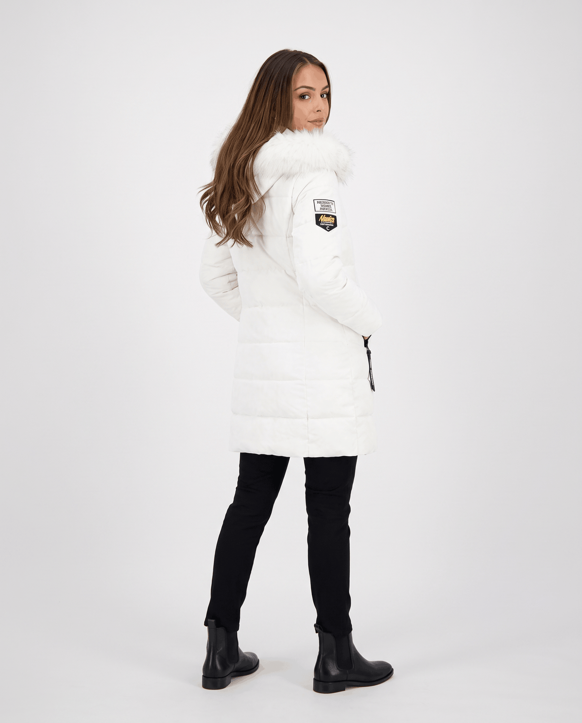 A woman wearing a white long parka jacket with an insulated design, hood, and full-zip front, side view