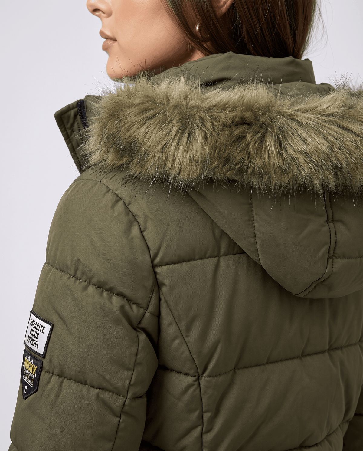 Close-up of a woman wearing a long olive green parka jacket, showing the fur-trimmed hood and quilted insulation