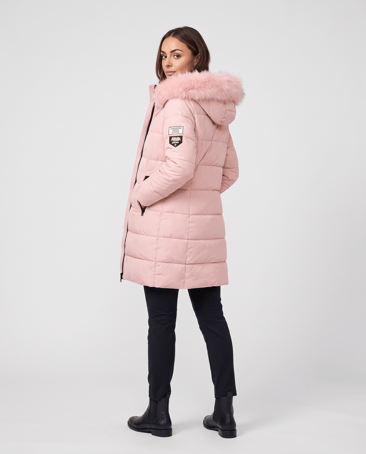 A woman wearing a long pink insulated parka jacket with a hood and full-zip front, shown from the back