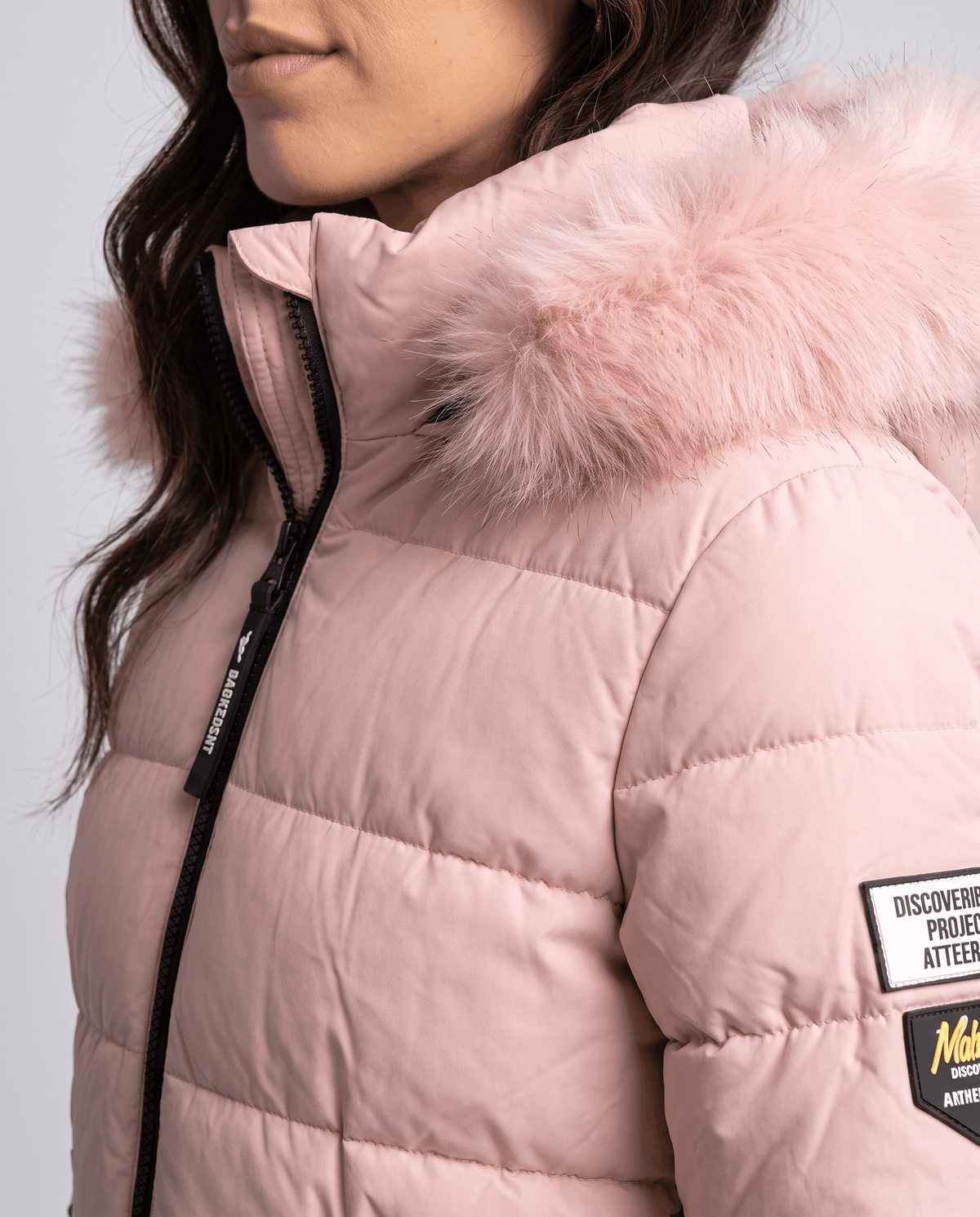 Close-up of a woman wearing a long pink insulated parka jacket, showing the fur-trimmed hood and quilted insulation
