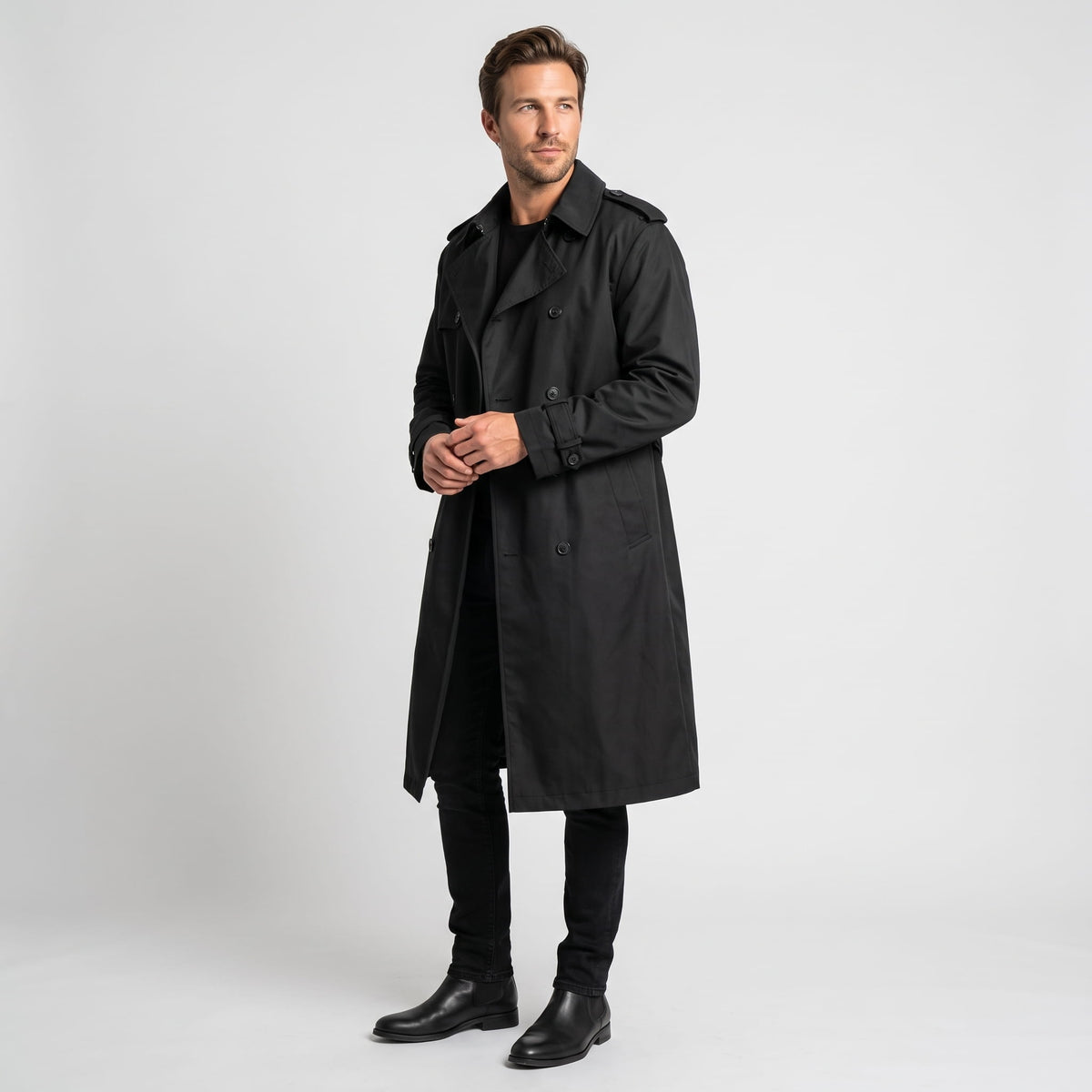 A man wearing a black long trench coat with a double-breasted front and waist belt, shown from the front