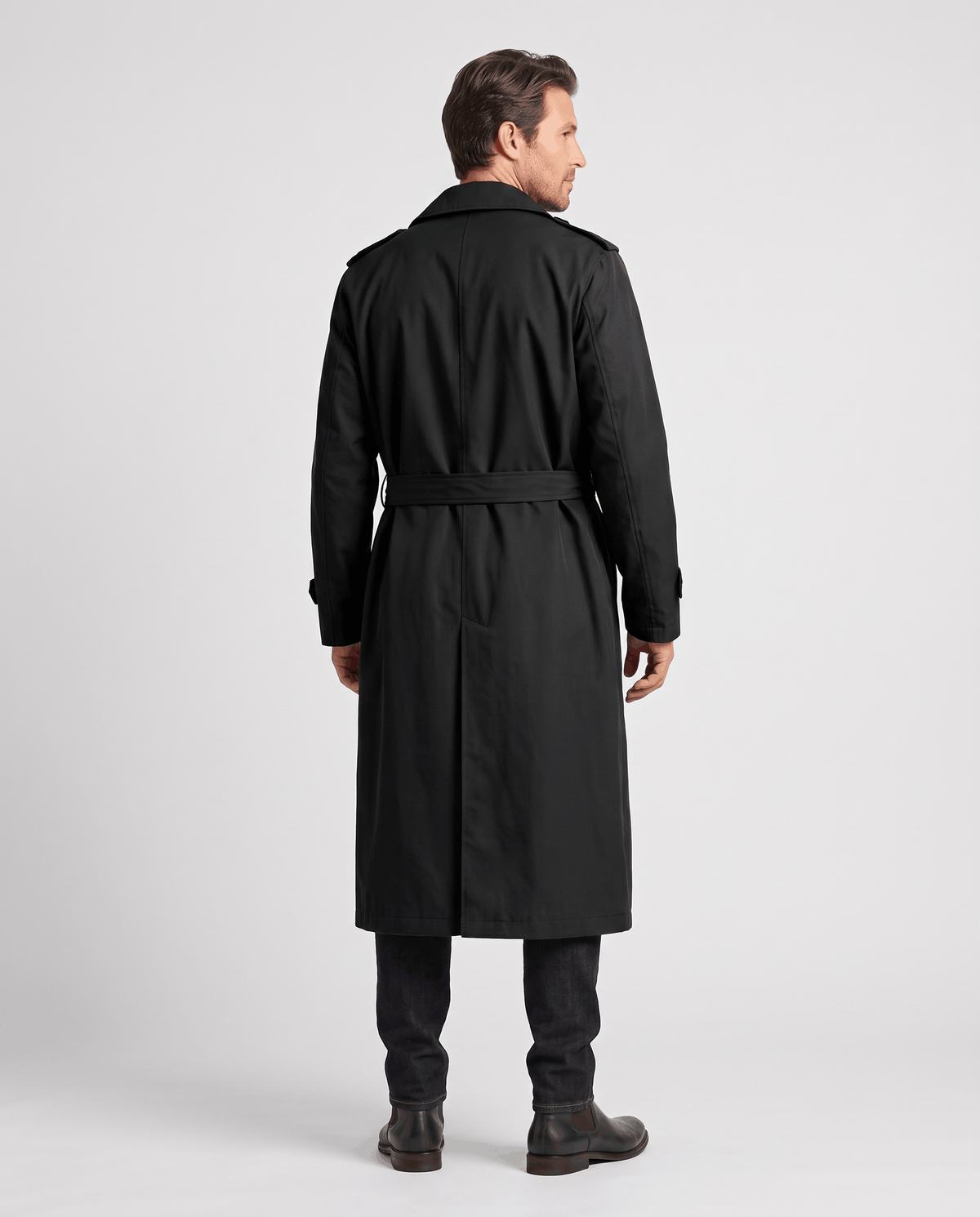 A man wearing a black long trench coat with a double-breasted front and waist belt, shown from the back
