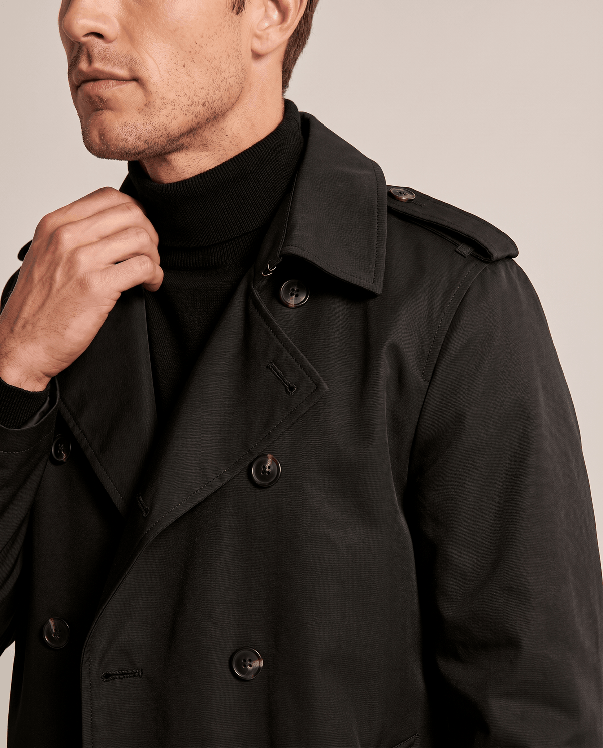 Close-up of a man wearing a black double-breasted trench coat, showing the wide lapels, collar, and front buttons