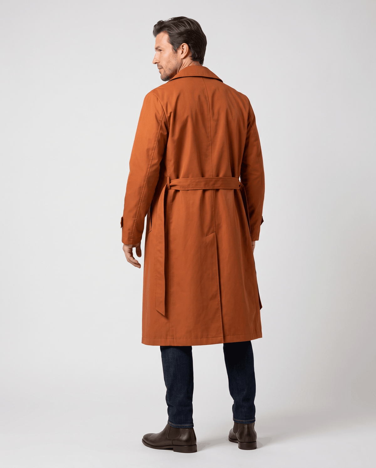 A man wearing an orange long trench coat with a double-breasted front and waist belt, shown from the back