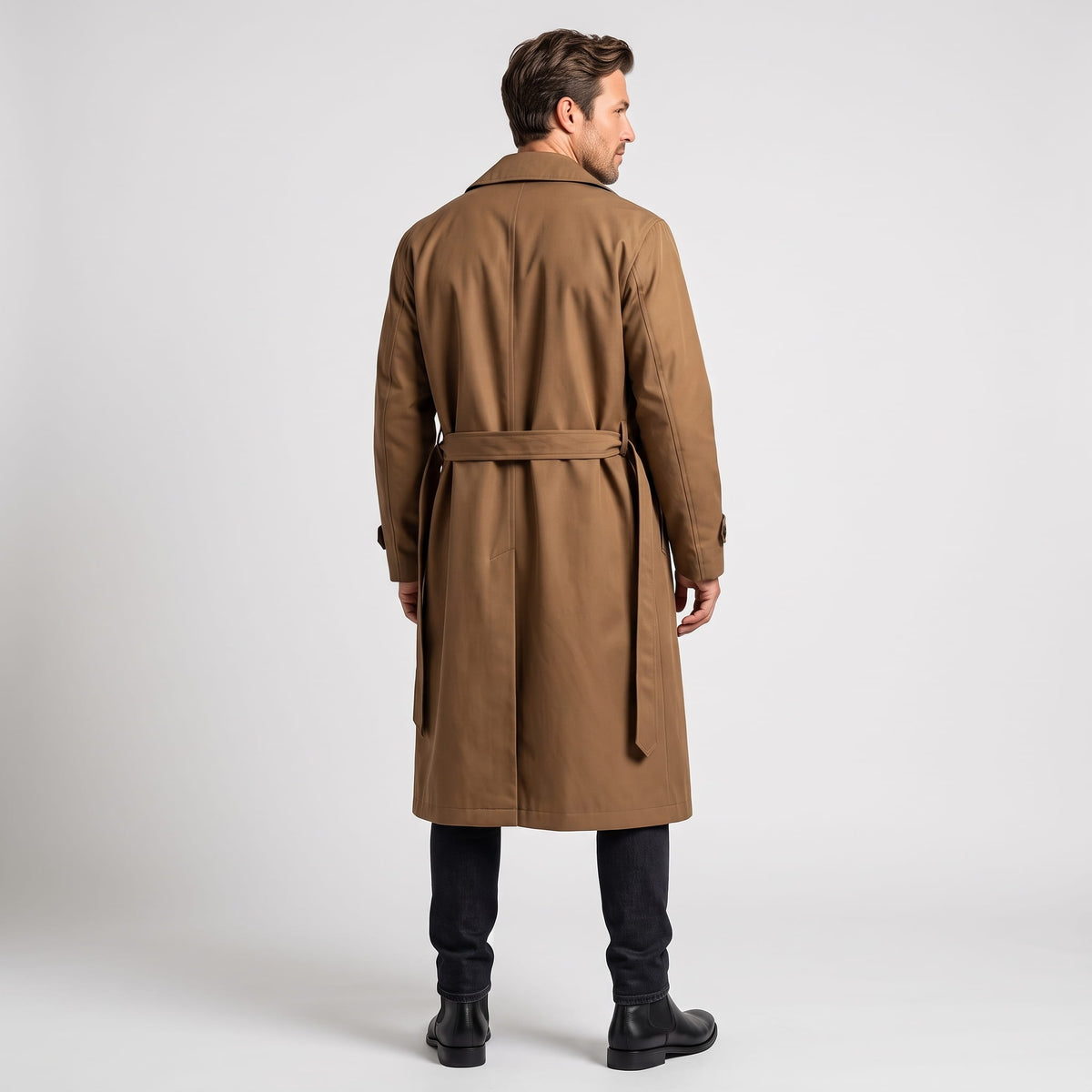 A man wearing a long brown trench coat with a double-breasted front and waist belt, shown from the back