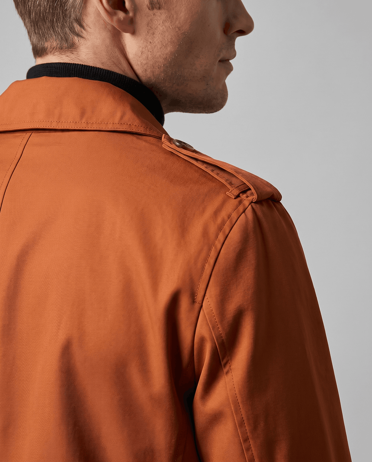 Close-up of an orange long trench coat showing the structured collar, shoulder detail, and smooth fabric