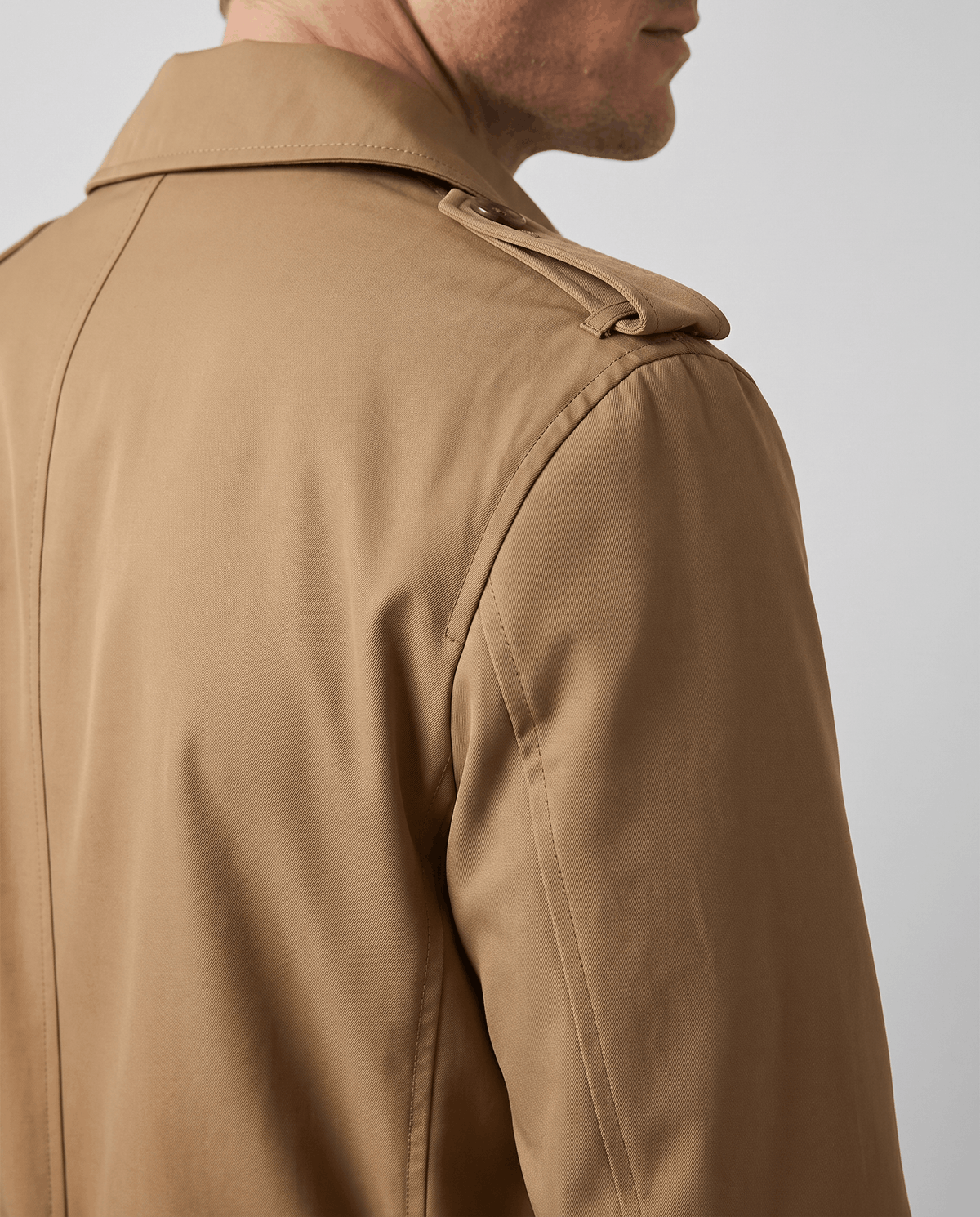 Close-up of a brown trench coat showing the shoulder detail, structured collar, and smooth fabric