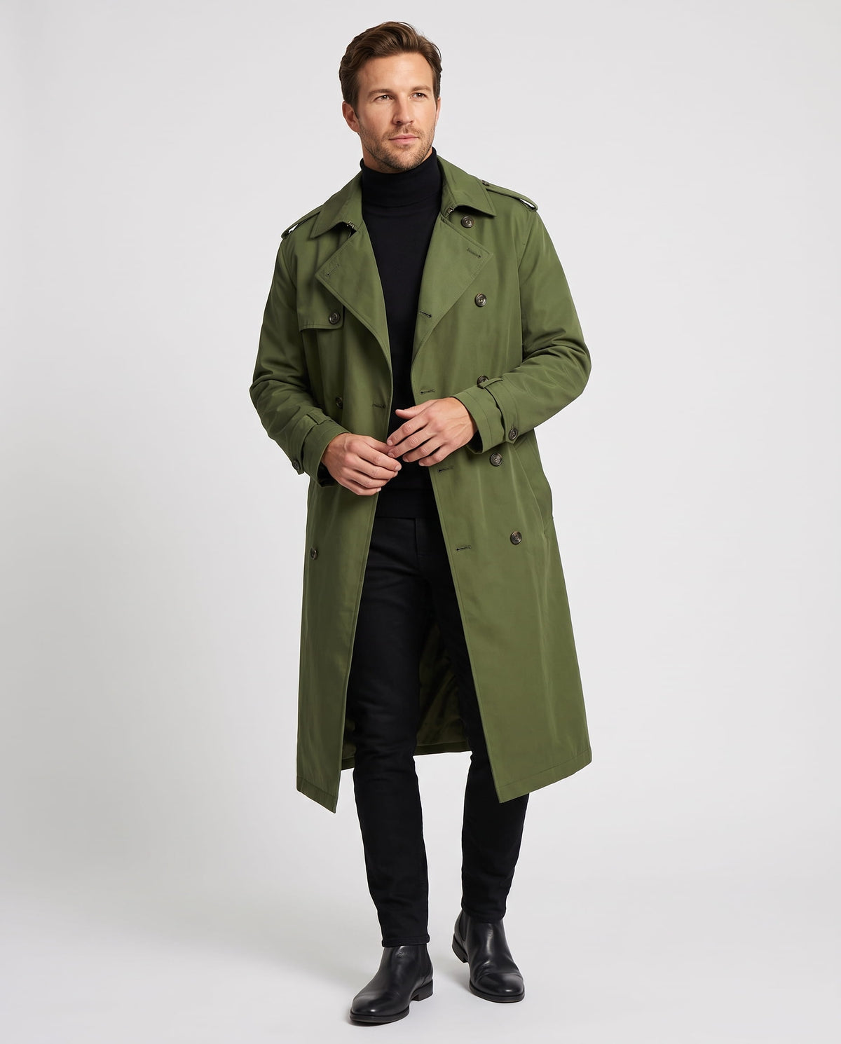 A man wearing a long olive green trench coat with a double-breasted front and waist belt