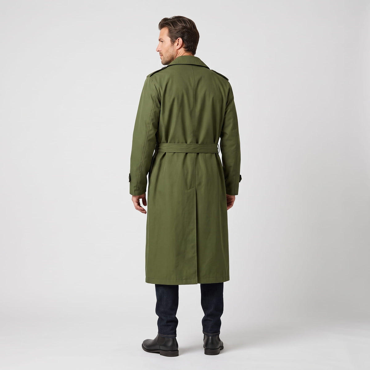 A man wearing a long olive green trench coat with a double-breasted front and waist belt, shown from the back