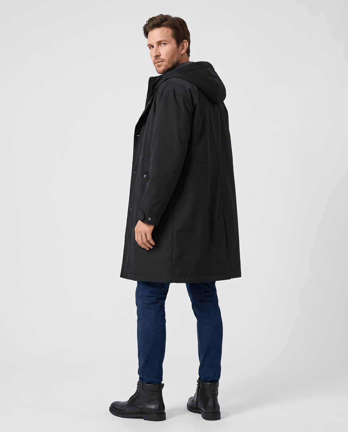 A man wearing a longline black hooded trench coat with a full-length design, shown in side view