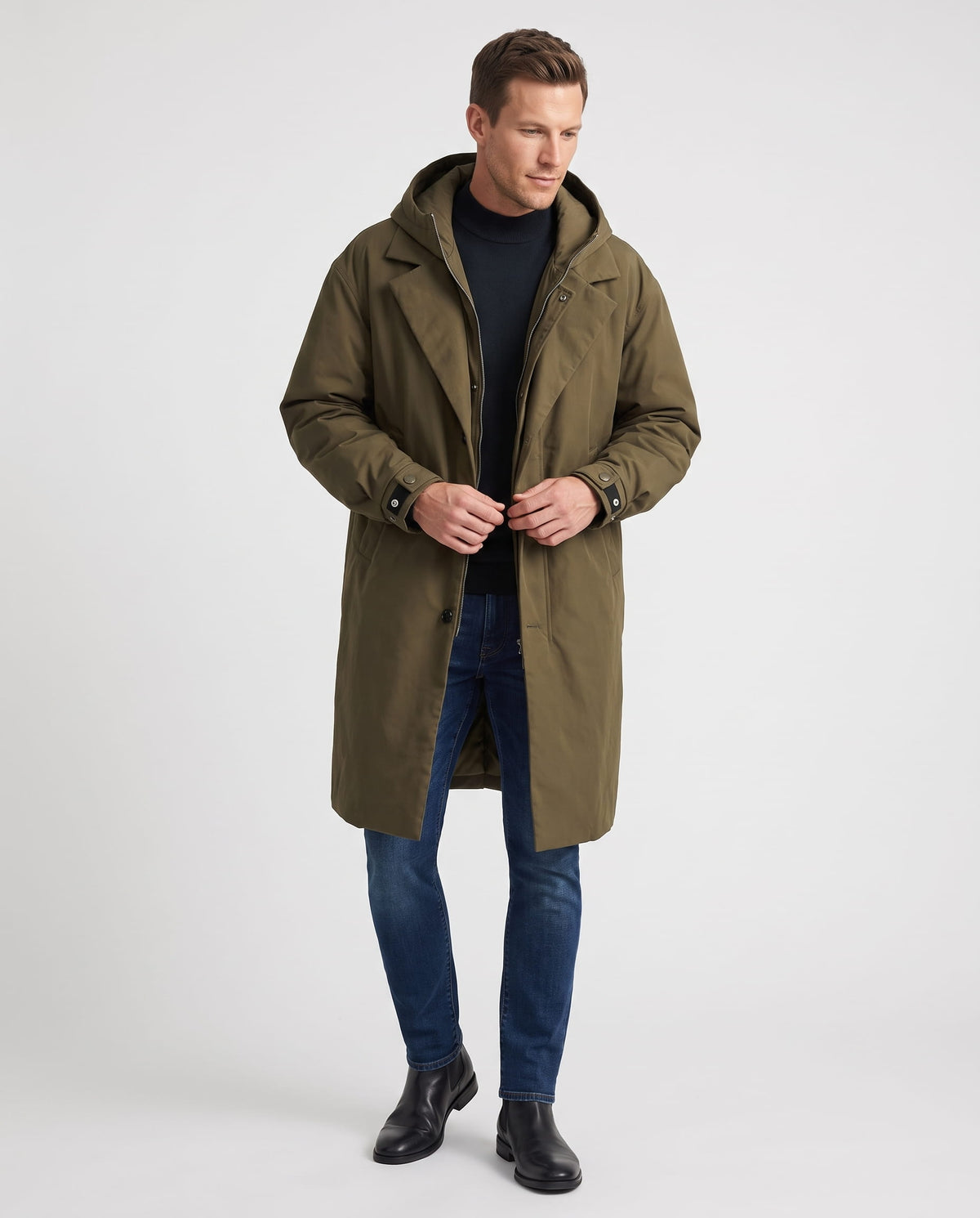 A man wearing a longline olive green trench coat with a hood and full-length design