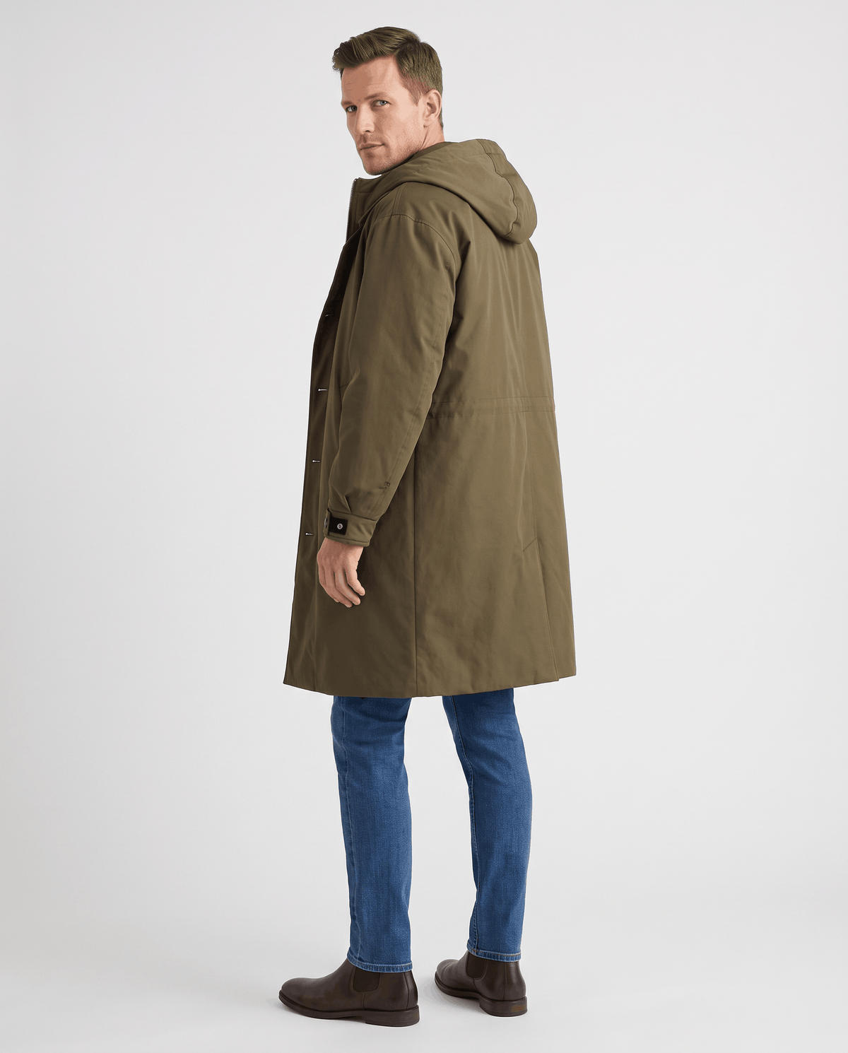 A man wearing a longline olive green hooded trench coat, shown from the back
