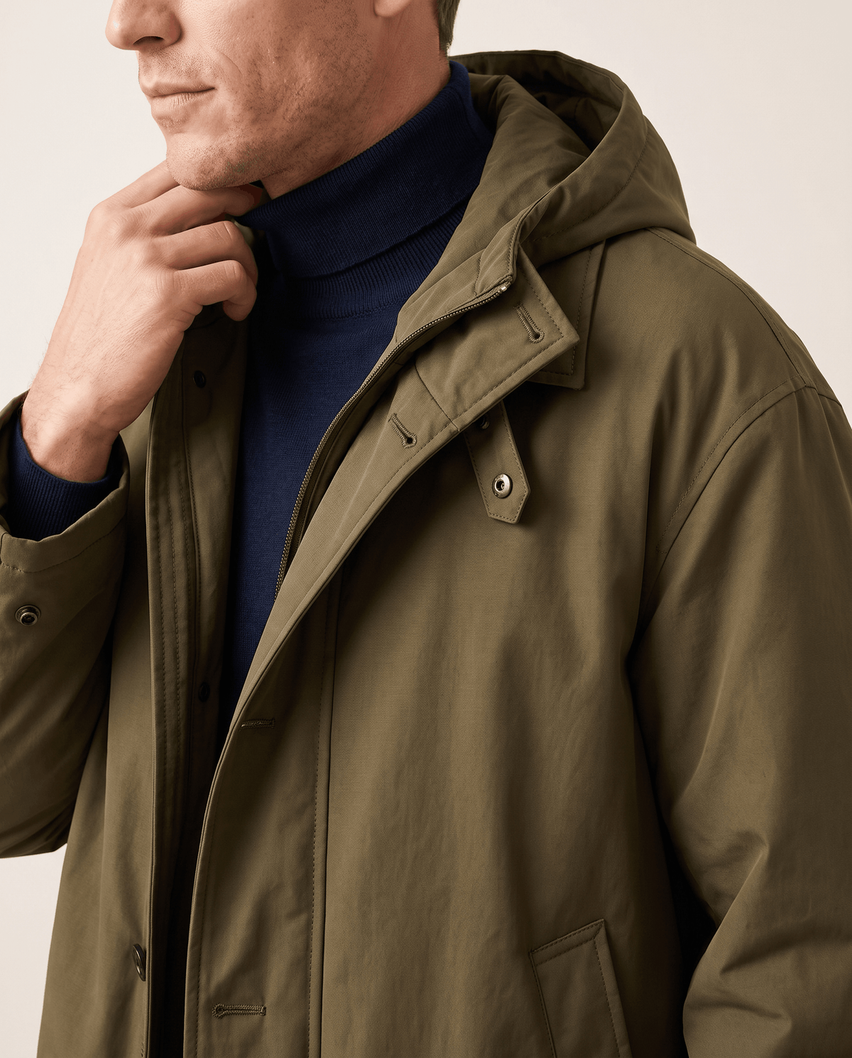 Close-up of a man wearing an olive green longline trench coat, showing the hood, collar, and front closure