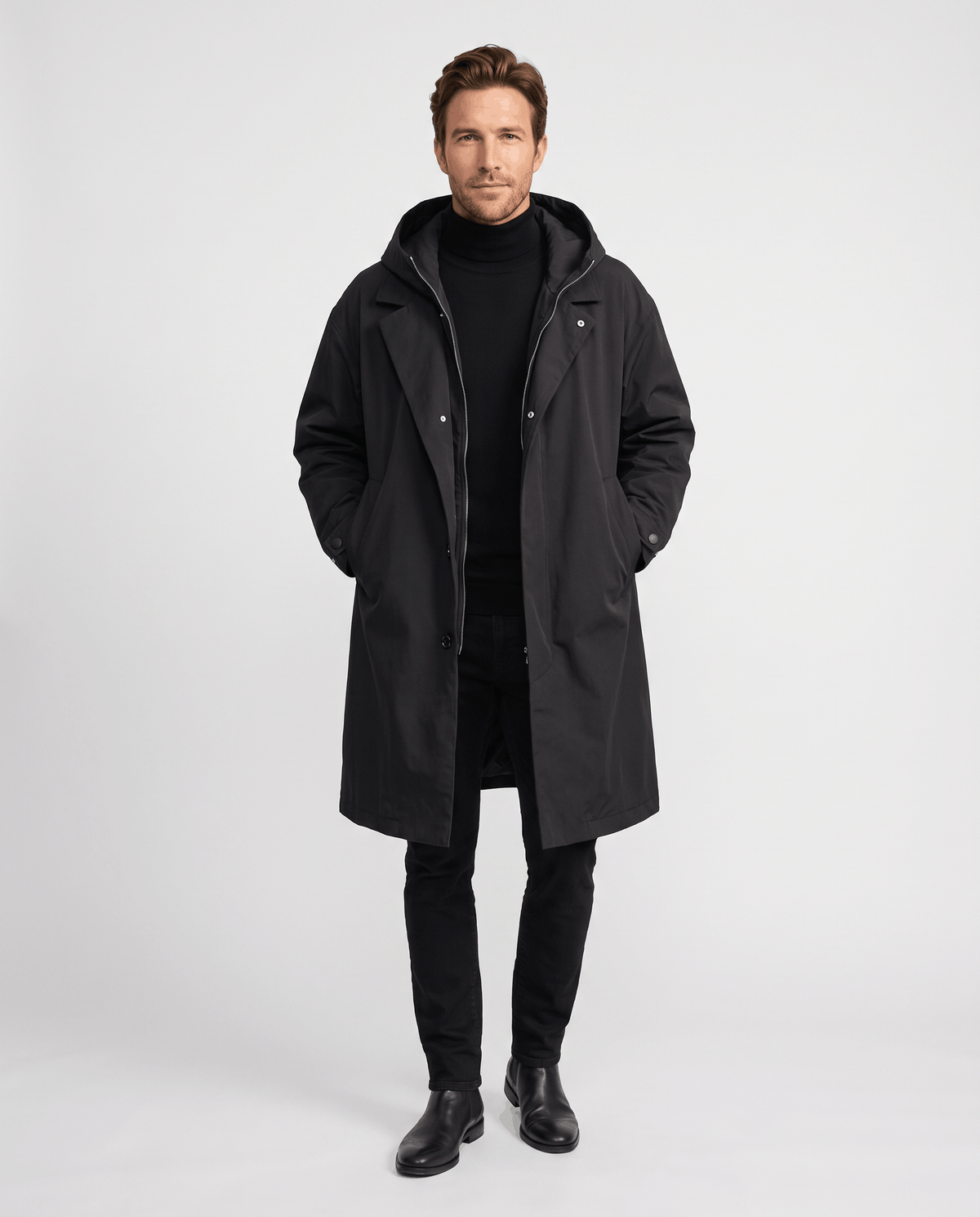 A man wearing a longline black trench coat with a hood, full-length design, and weather-resistant outer layer