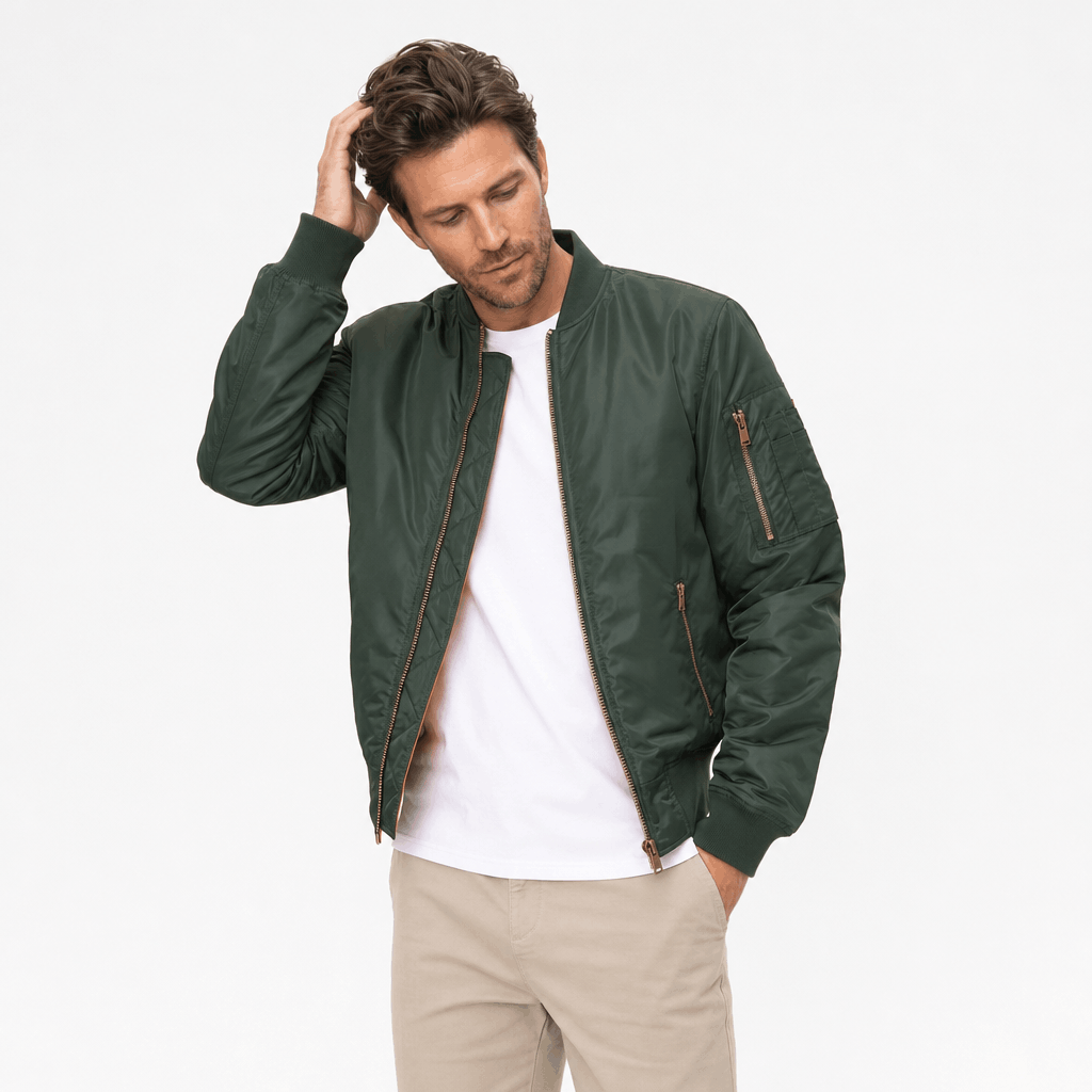 Male model wearing a dark green bomber jacket over a white shirt with light-colored pants.