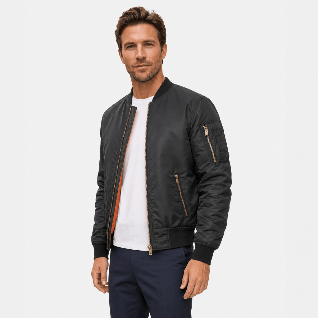 Male model wearing a black bomber jacket with ribbed cuffs, zippered side pockets, and an orange zipper lining.
