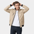 Male model wearing a beige utility-style zip-up jacket over a white T-shirt with dark blue jeans.