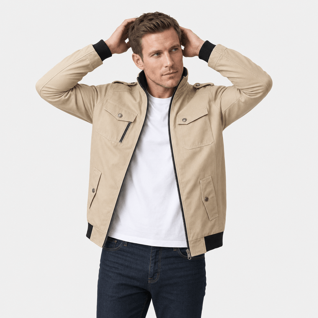 Male model wearing a beige utility-style zip-up jacket over a white T-shirt with dark blue jeans.