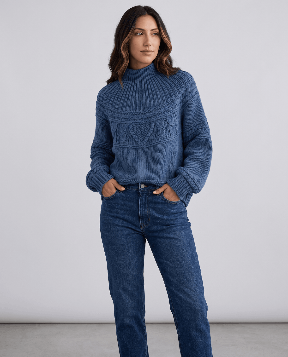 Blue Merino Wool Cable Knit Sweater worn by a female model with blue jeans, featuring a relaxed fit, textured cable knit pattern, high neckline, long sleeves, and ribbed trim.