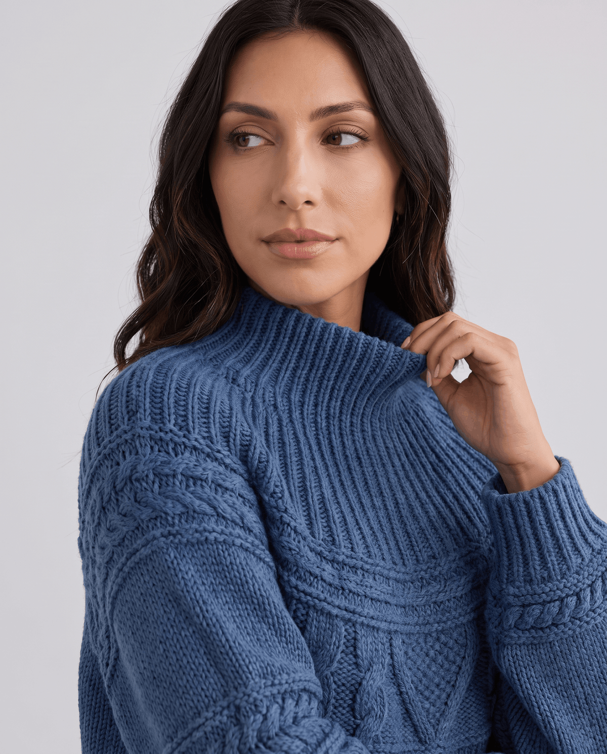 Blue Merino Wool Cable Knit Sweater worn by a female model, shown in close-up with a high neckline, textured cable knit pattern, and relaxed fit.