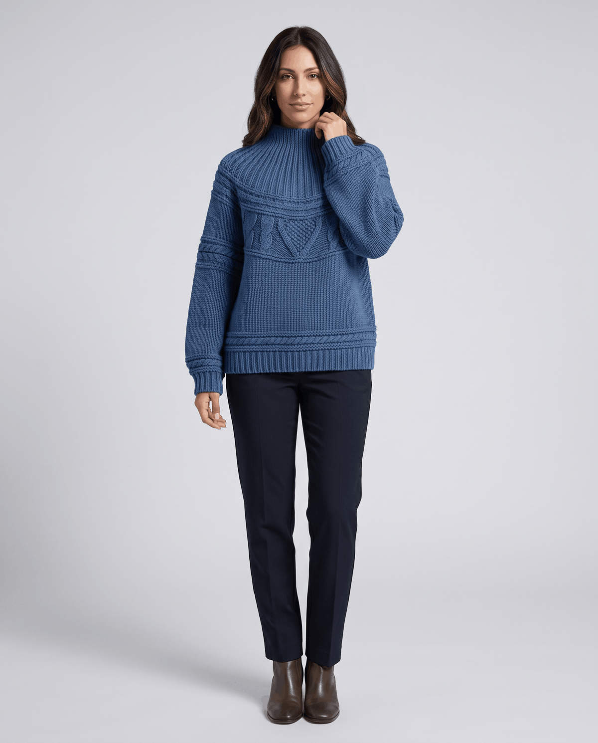 Blue Merino Wool Cable Knit Sweater worn by a female model with dark pants, featuring a relaxed fit, textured cable knit pattern, high neckline, long sleeves, and ribbed trim.