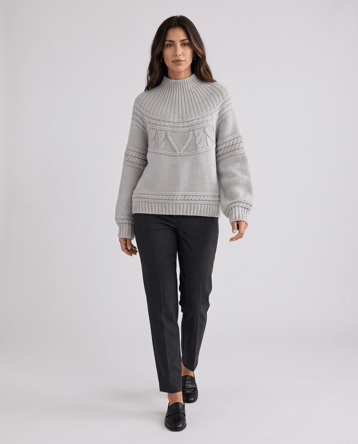 Gray Merino Wool Cable Knit Sweater worn by a female model with dark pants, featuring a relaxed fit, cable knit texture, long sleeves, and ribbed trim.