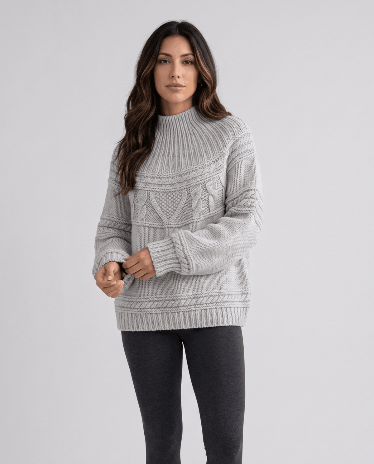 Gray Merino Wool Cable Knit Sweater worn by a female model, featuring a relaxed fit, textured cable knit pattern, high neckline, long sleeves, and ribbed trim.