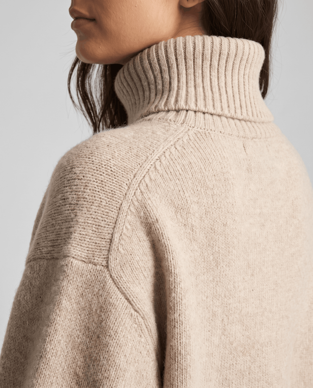 Dark Beige Merino Wool Turtleneck Sweater worn by a female model, shown in close-up with the high turtleneck collar and soft knit texture.