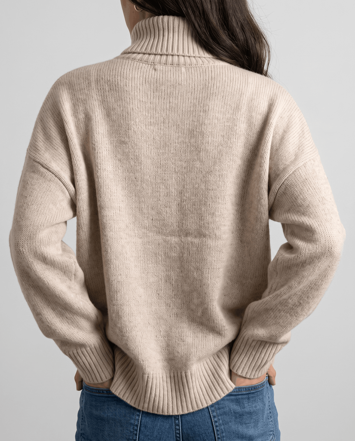 Dark Beige Merino Wool Turtleneck Sweater worn by a female model from the back, highlighting the oversized silhouette, high turtleneck collar, and ribbed cuffs.