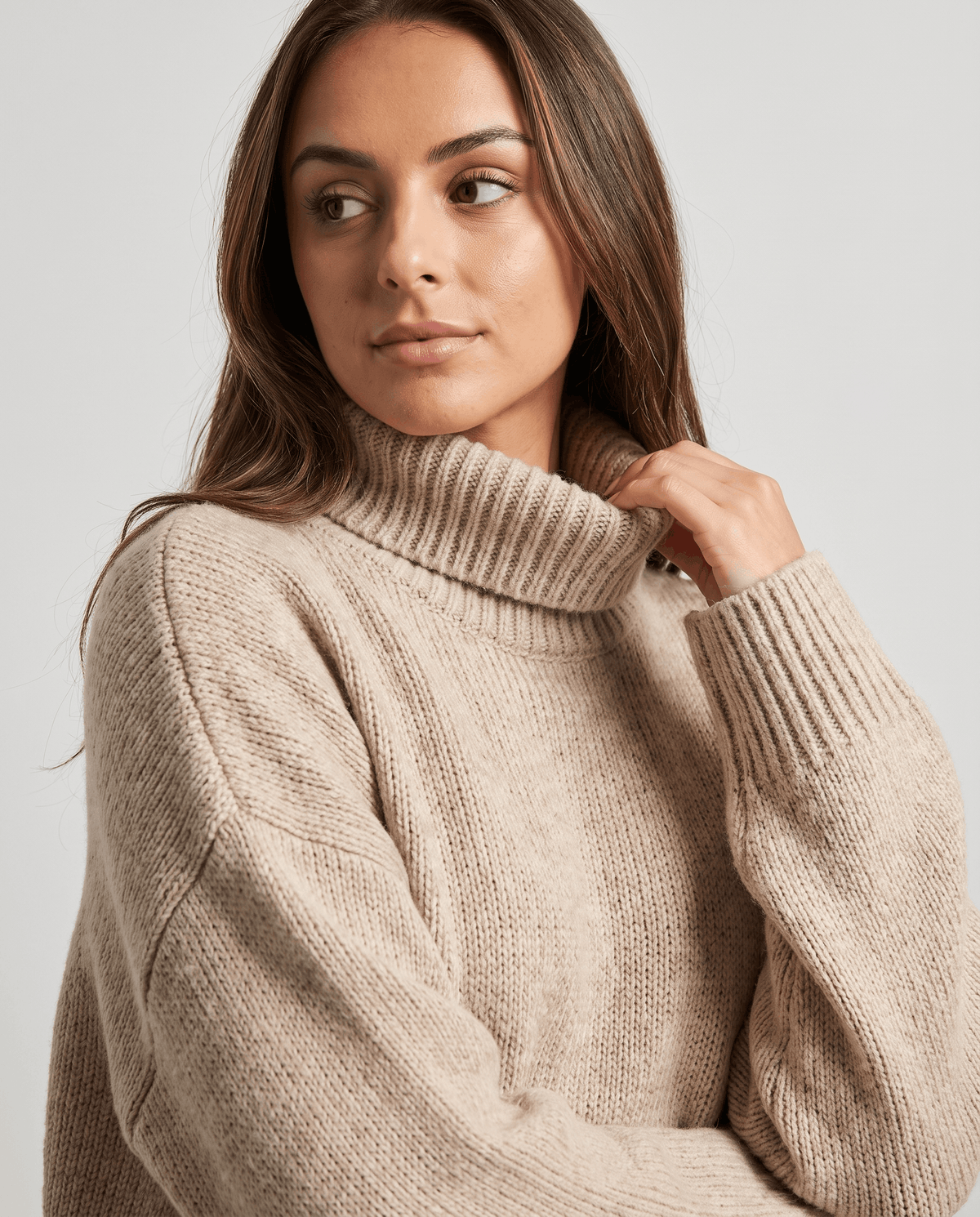 Beige Merino Wool Turtleneck Sweater worn by a female model, shown in close-up with a high turtleneck collar, soft knit texture, and oversized fit.