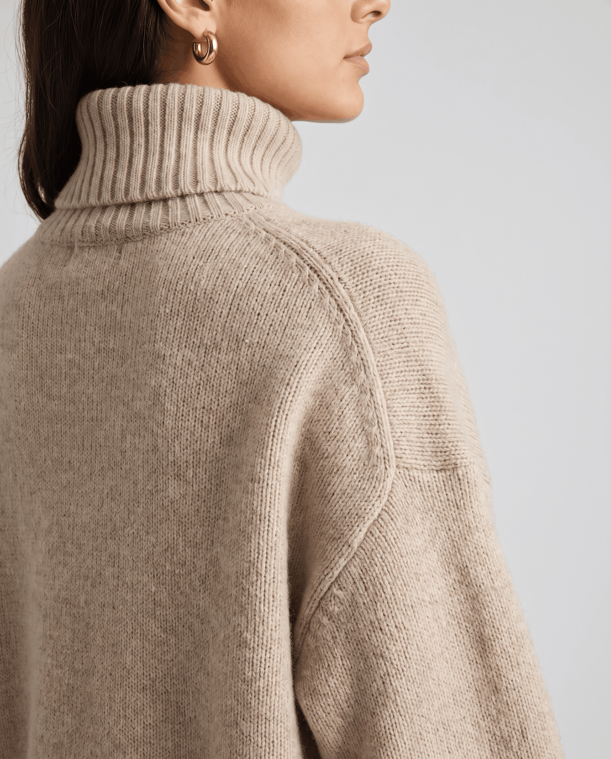 Beige Merino Wool Turtleneck Sweater worn by a female model, shown from the side with a high collar, relaxed oversized silhouette, and long sleeves.