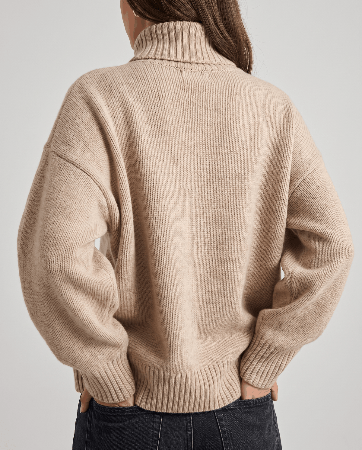 Beige Merino Wool Turtleneck Sweater worn by a female model from the back, showcasing the oversized fit, high turtleneck collar, and ribbed cuffs.