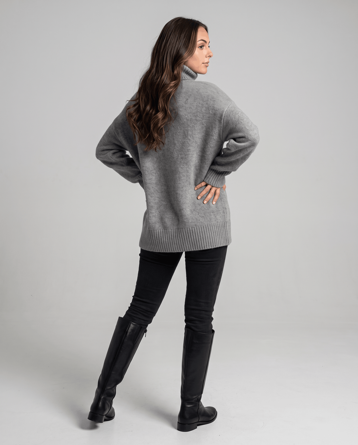 Gray Merino Wool Turtleneck Sweater worn by a female model from the back, highlighting the oversized silhouette, high turtleneck collar, and ribbed cuffs.