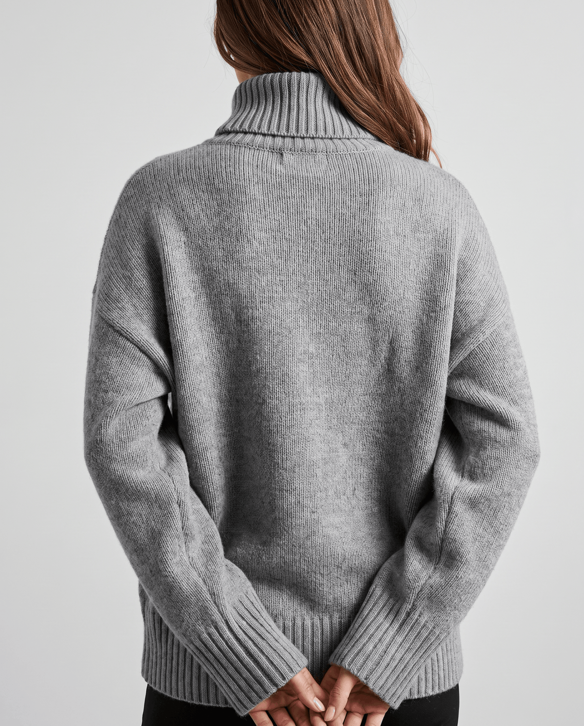 Gray Merino Wool Turtleneck Sweater worn by a female model, shown from the back in close-up, showcasing the soft knit texture, relaxed fit, and ribbed cuffs.