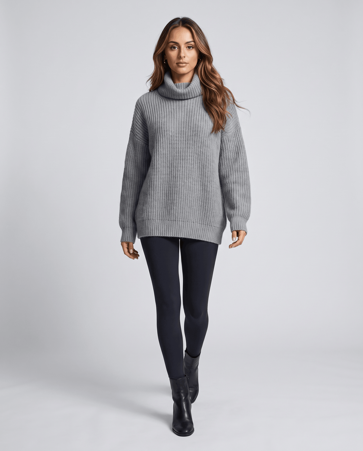 Gray Merino Wool Turtleneck Sweater worn by a female model with dark leggings, featuring an oversized fit, high turtleneck collar, long sleeves, and ribbed cuffs.