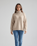 Beige Merino Wool Turtleneck Sweater worn by a female model, featuring an oversized fit, high turtleneck collar, long sleeves, and ribbed cuffs.