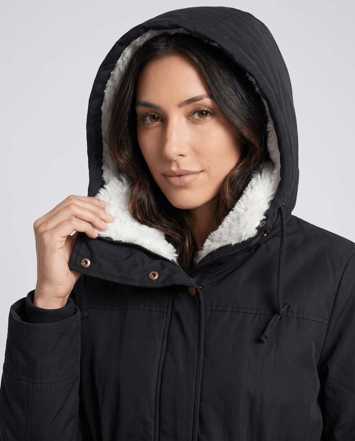 A woman wearing a black mid-length parka jacket with a fur-trimmed hood and drawstring waist, close-up view