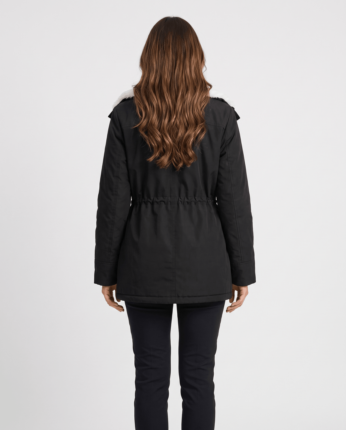 A woman wearing a black mid-length parka jacket with a fur-trimmed hood and drawstring waist, shown from the back