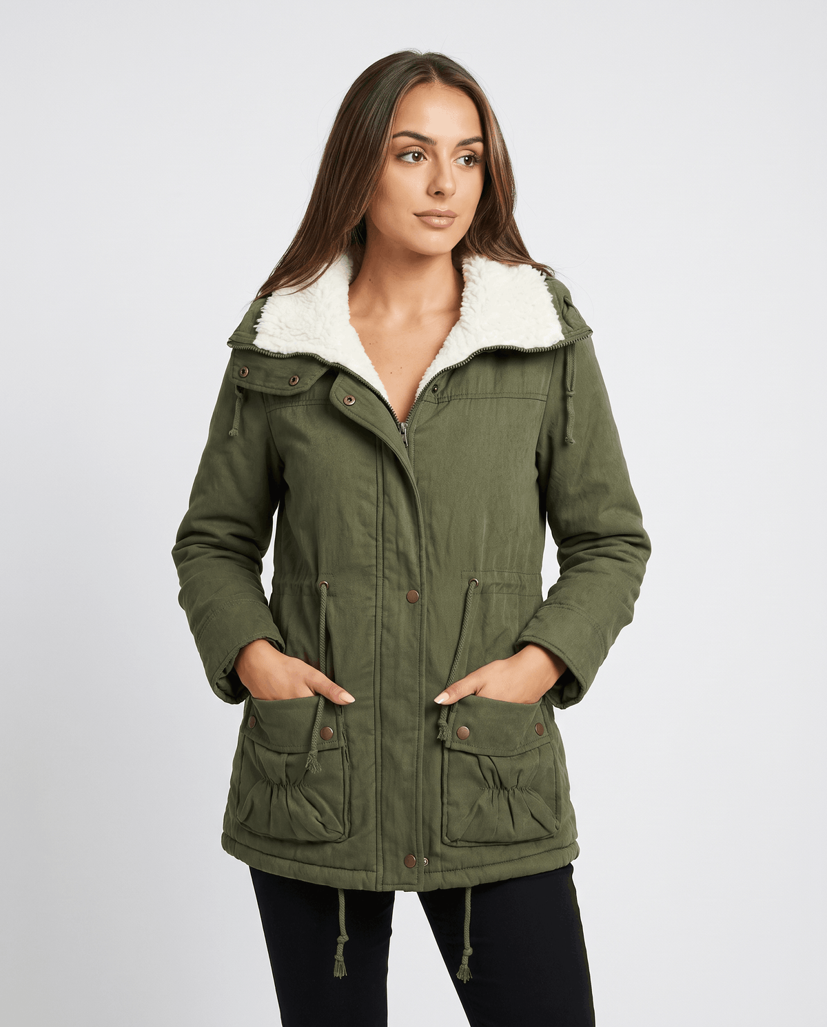 A woman wearing a mid-length olive green parka jacket with a fur-trimmed hood, drawstring waist, and front pockets