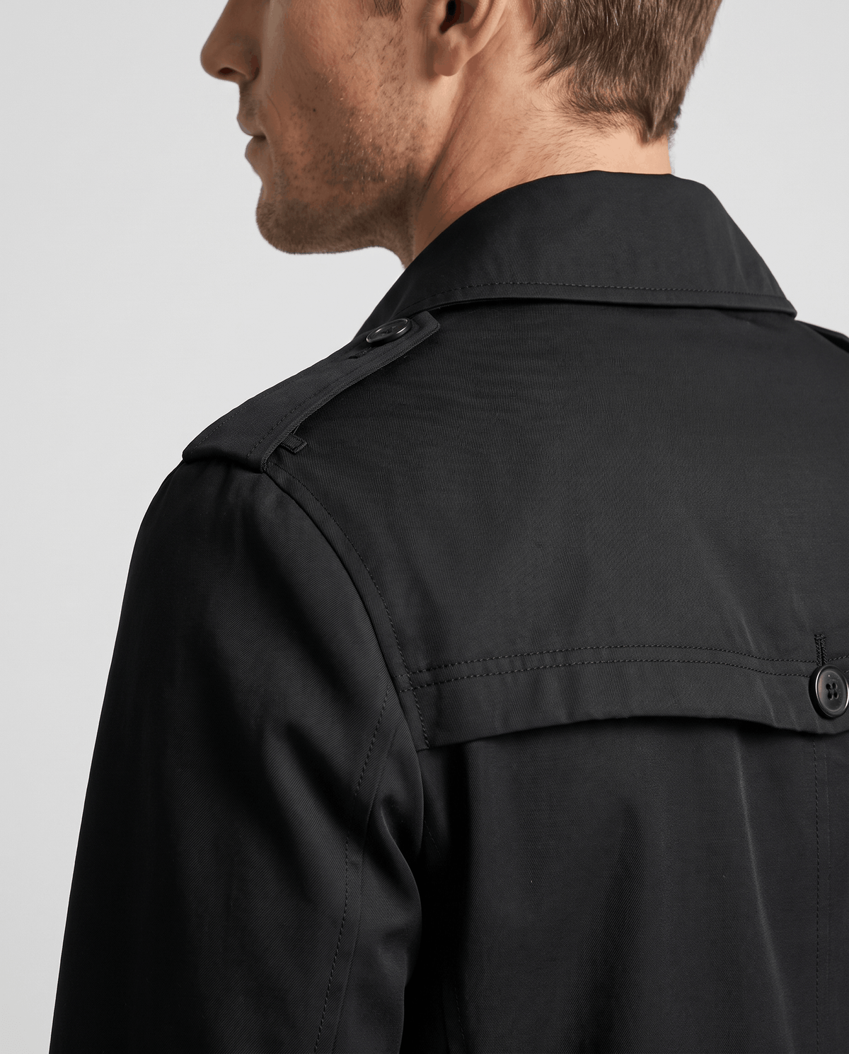 Close-up of a man wearing a black mid-length single-breasted trench coat, showing the collar and back detail