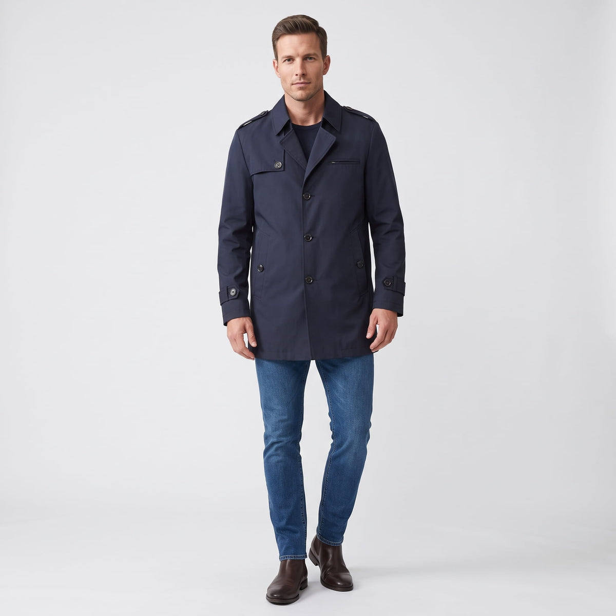 A man wearing a navy blue mid-length single-breasted trench coat with a button front, full-body front view