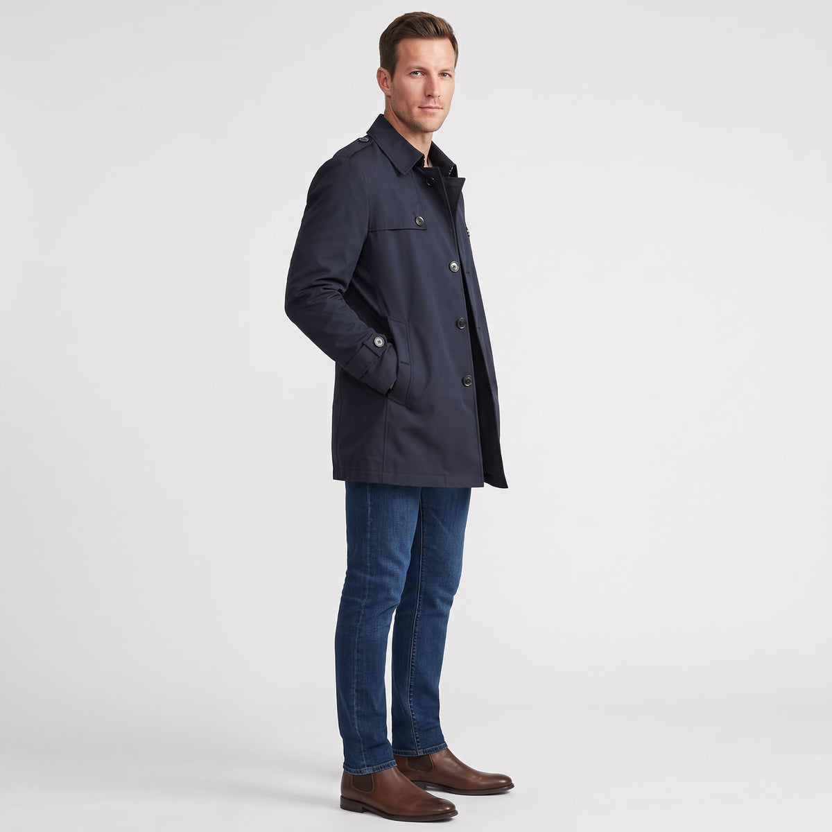 A man wearing a navy blue mid-length single-breasted trench coat with a button front, side view