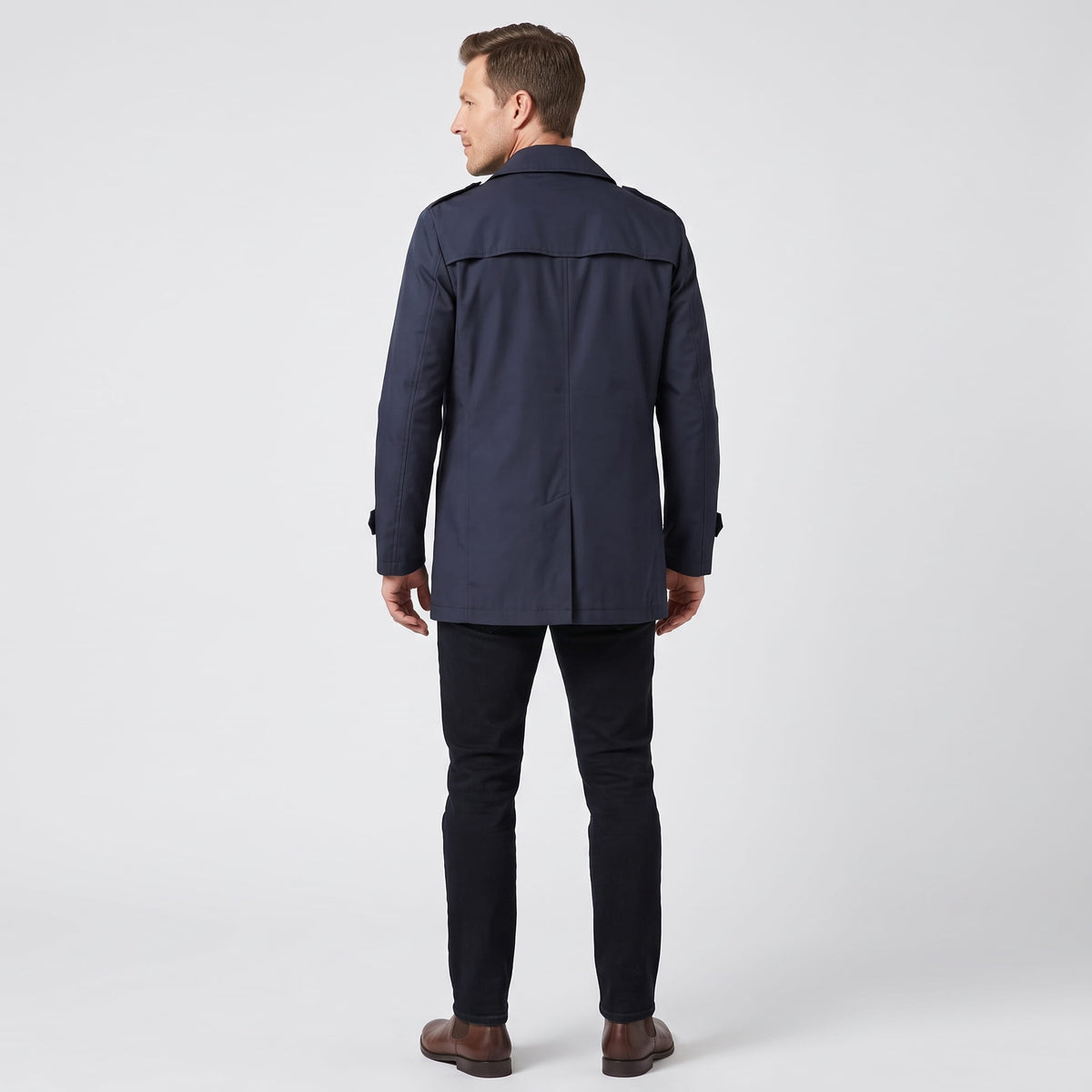 A man wearing a navy blue mid-length single-breasted trench coat with a button front, back view