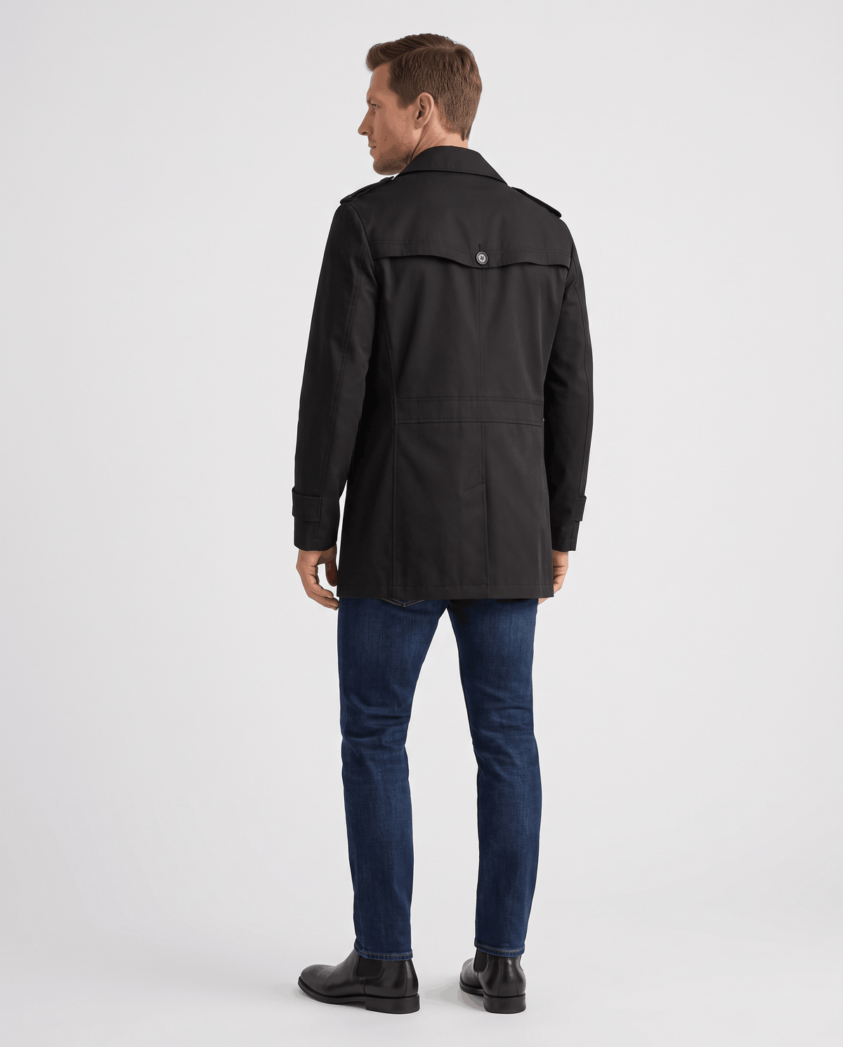 A man wearing a black mid-length single-breasted trench coat, shown from the back
