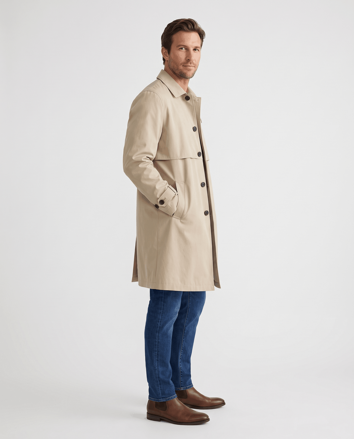 A man wearing a beige mid-length single-breasted trench coat with a button front and clean lines, side view