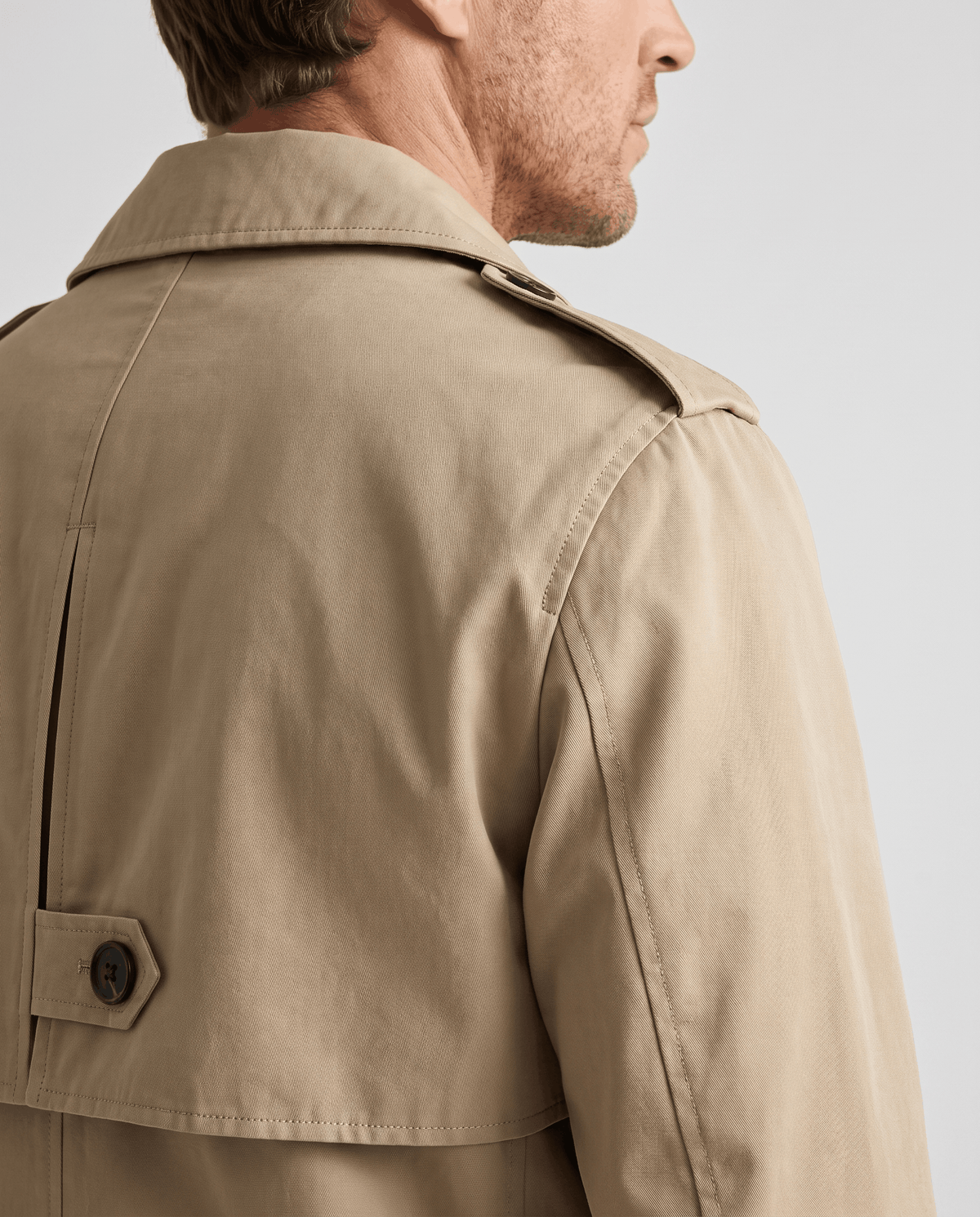 Close-up of a man wearing a beige mid-length single-breasted trench coat, showing the collar and back detail